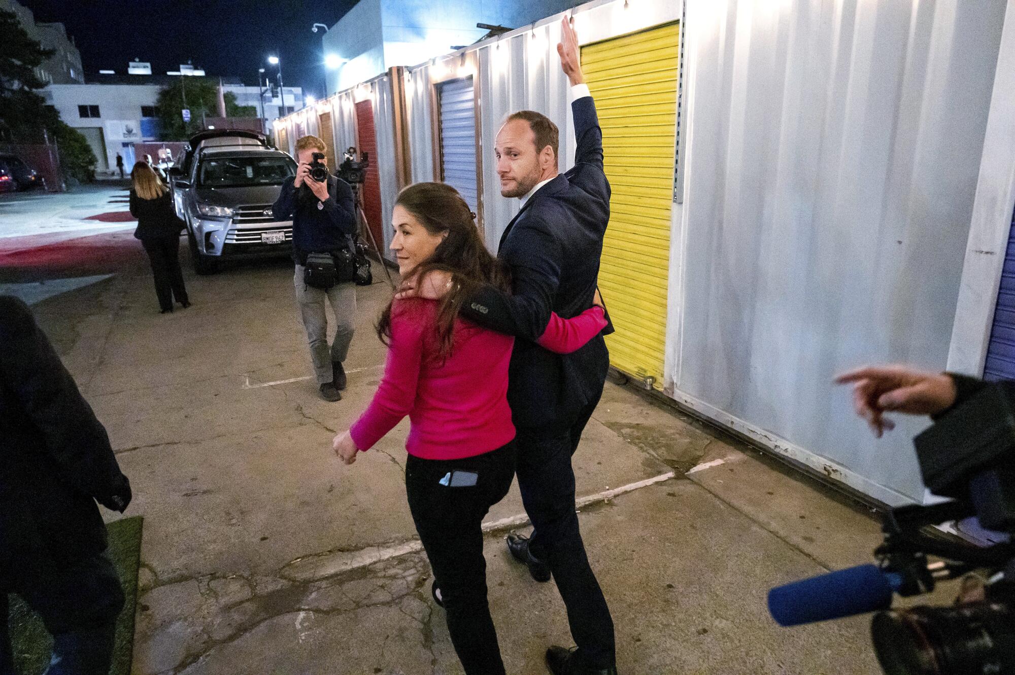 Chesa Boudin and his wife wave to news cameras while walking together