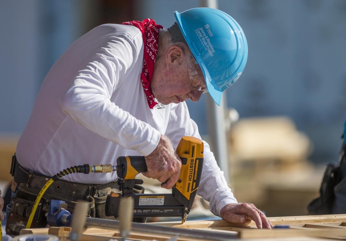 Former President Carter wearing a hard hat and using a drill at a building site.