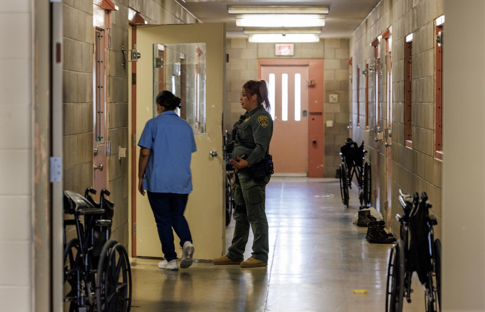 A woman walks through a door with a guard watching.