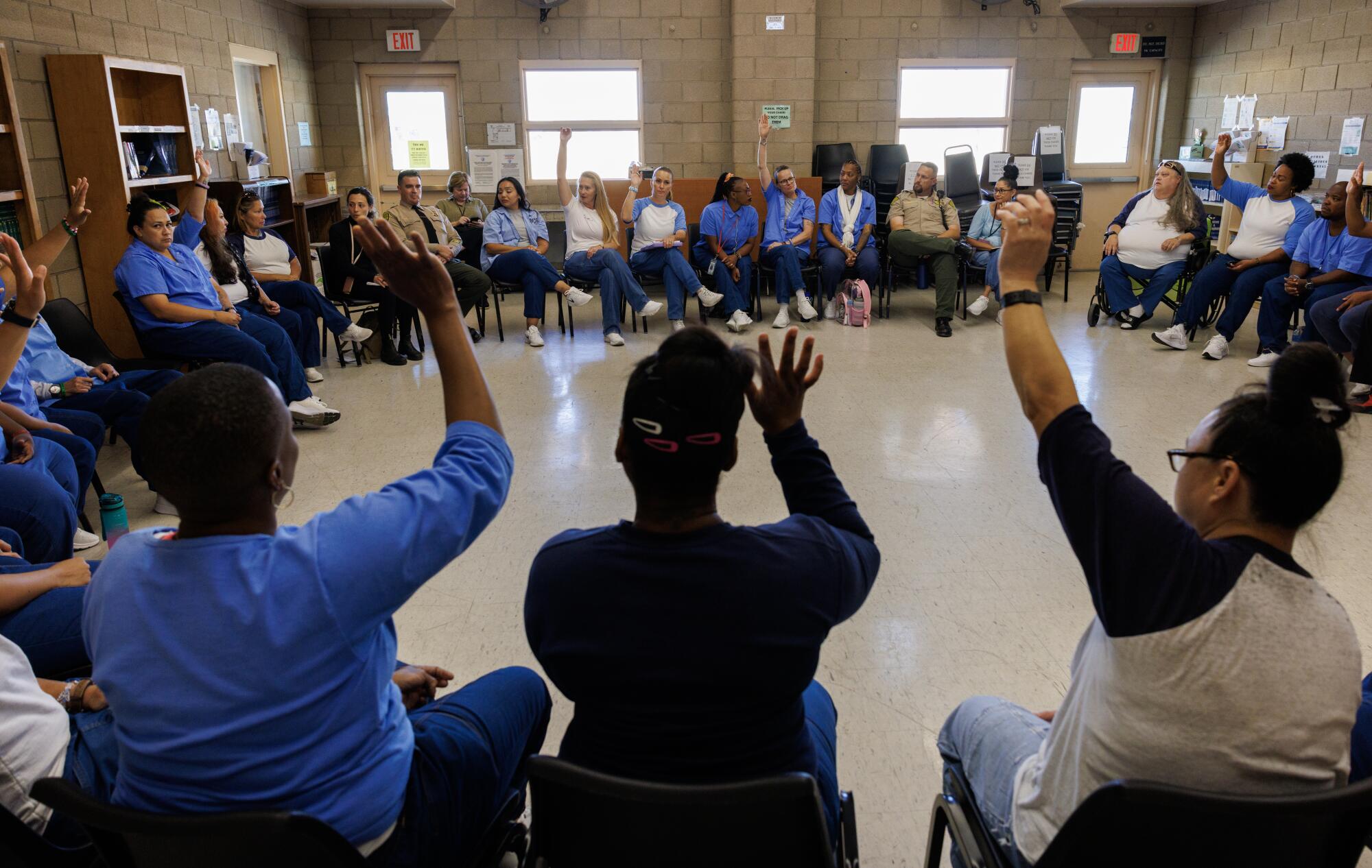 Many women seated in a circle raise their hands.